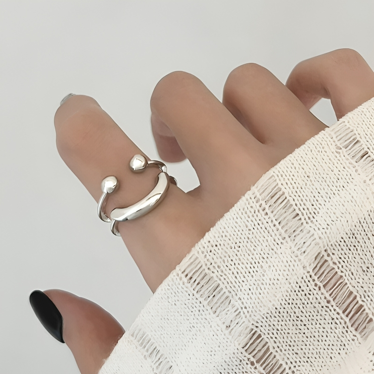 Bague sourire argentée portée à l'index, vue de près, avec une manche en maille blanche au premier plan. 3
