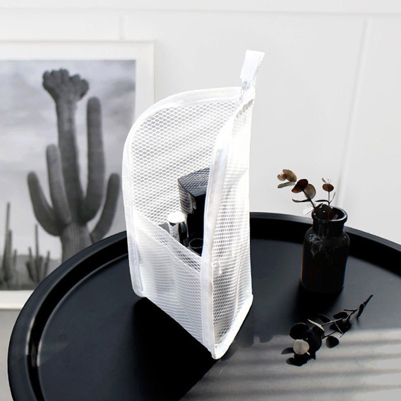 Pochette blanche en filet ajouré posée debout sur une table ronde noire, produits de beauté visibles à l'intérieur, décor épuré. 2