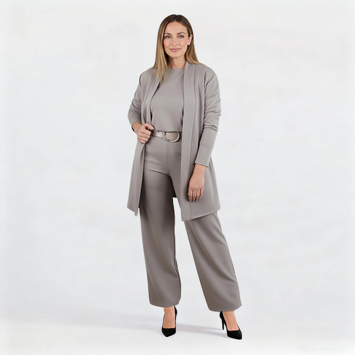 Ensemble gris taupe porté par une mannequin en pied sur fond blanc, cardigan entrouvert, ceinture à boucle ronde, escarpins noirs. 11