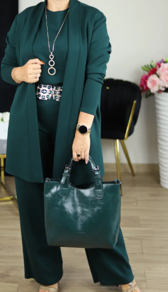Femme portant l'ensemble vert foncé avec collier à anneaux et ceinture ornée, tenant un sac assorti, devant un fauteuil noir et or. 17