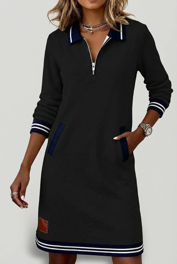 Robe noire portée de face par un mannequin, une main dans la poche, col polo bleu marine rayé et ourlet rayé. 11