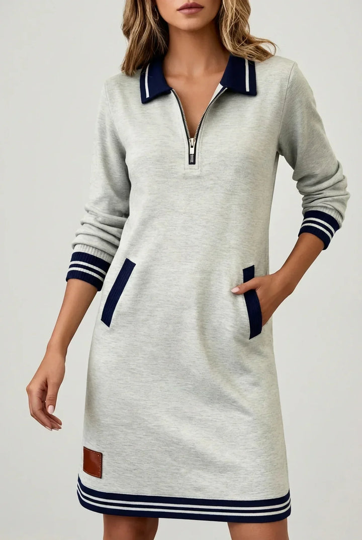 Robe gris clair portée par un mannequin en vue de face sur fond neutre, zip au col, écusson brun à l'ourlet. 7