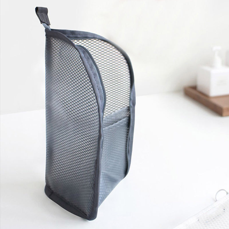 Pochette grise en filet posée verticalement sur un plan blanc, vue de profil avec sa poche extérieure et sa languette de suspension. 7