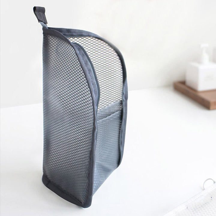 Pochette grise en filet posée verticalement sur un plan blanc, vue de profil avec sa poche extérieure et sa languette de suspension. 7