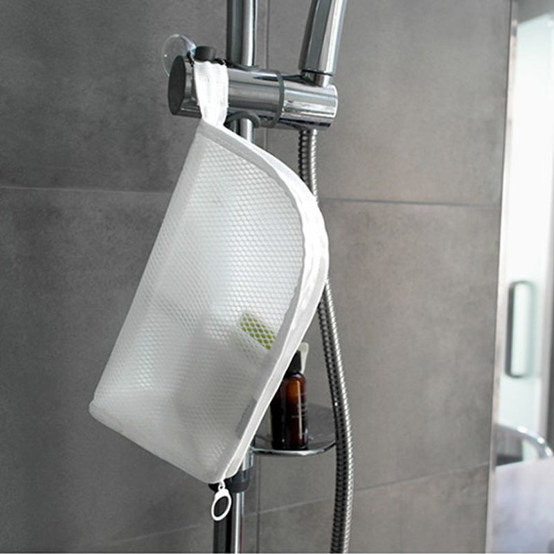 Pochette blanche en filet suspendue par sa languette à la barre de douche d'une salle de bain, flacon posé sur l'étagère. 4