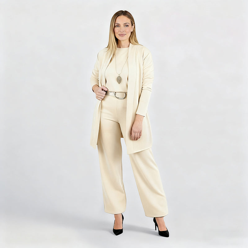 Ensemble crème porté par une mannequin en pied sur fond blanc, avec pendentif en forme de feuille, ceinture et escarpins noirs. 14