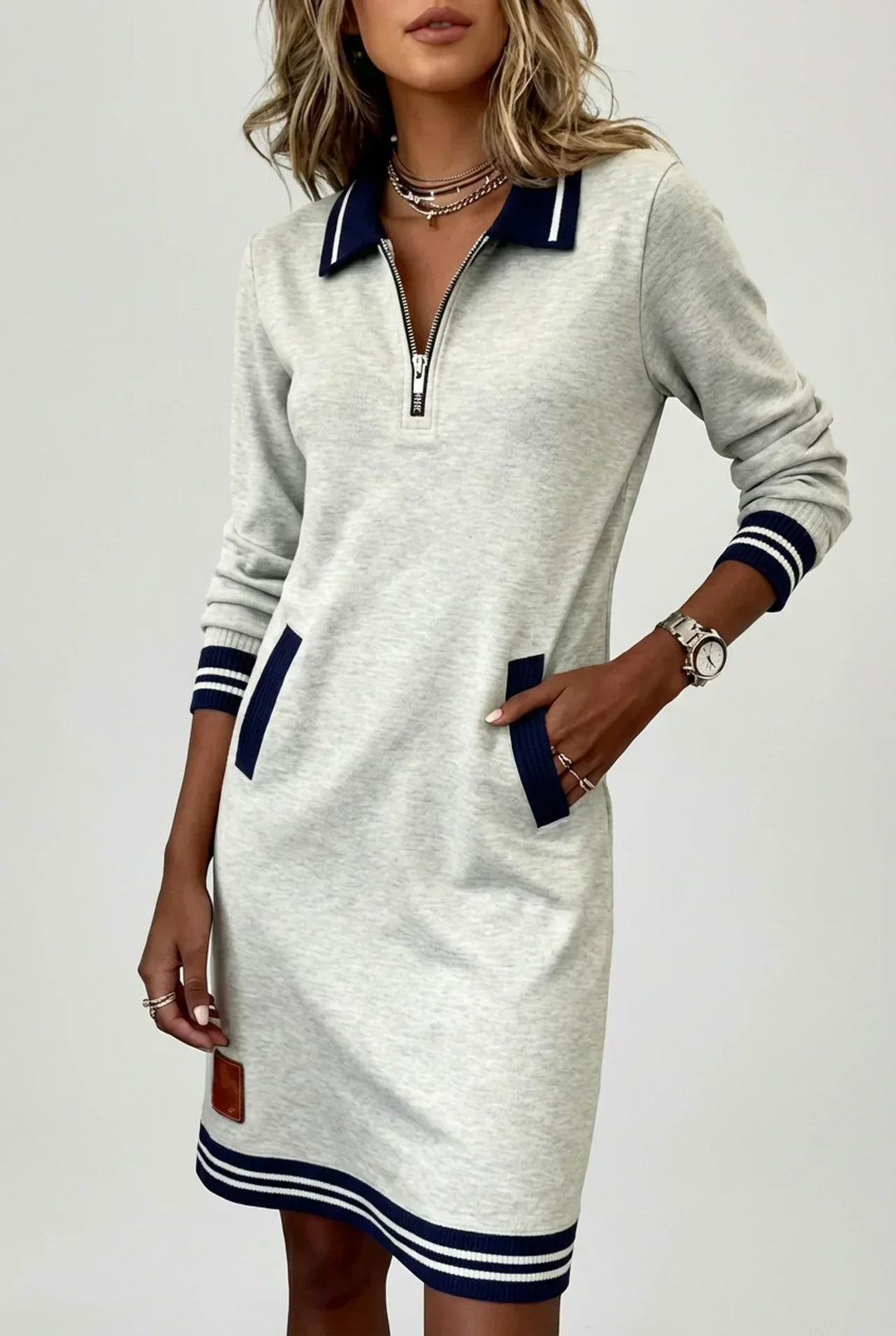 Robe grise chinée portée en plan large par un mannequin, main dans la poche, fond clair, ourlet à rayures bleu marine. 6