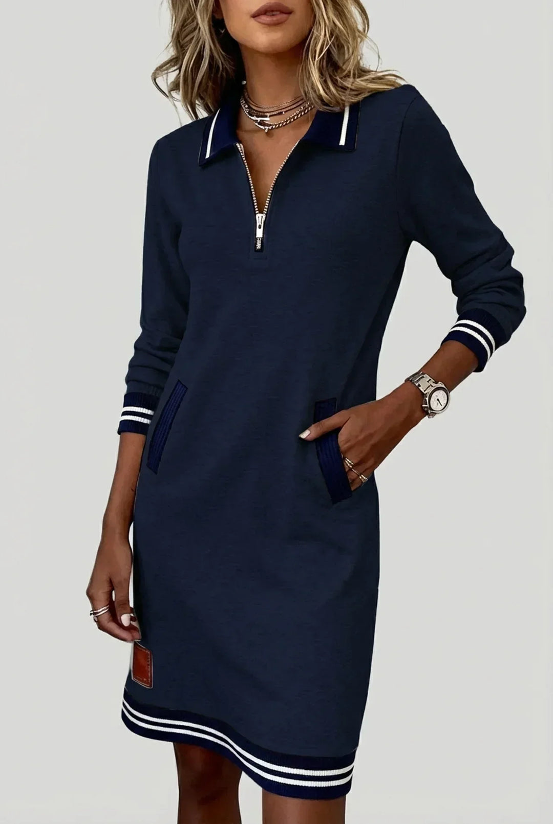 Robe bleu marine à zip devant et bords rayés, portée par un mannequin, une main dans la poche, petit écusson brun. 3