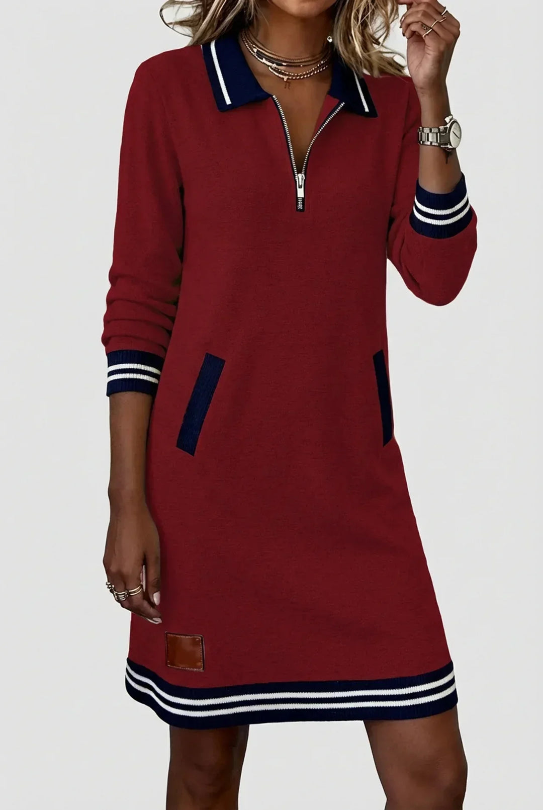 Robe rouge bordeaux portée par un mannequin, main relevée, col polo rayé bleu marine et écusson brun près de l'ourlet. 12
