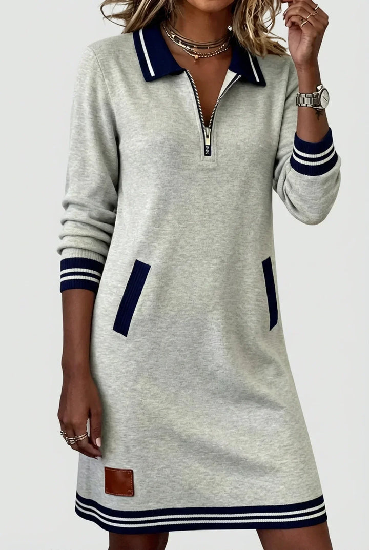 Robe grise à col polo bleu marine rayé, portée par un mannequin, main relevée près du visage, poches soulignées de bleu. 1