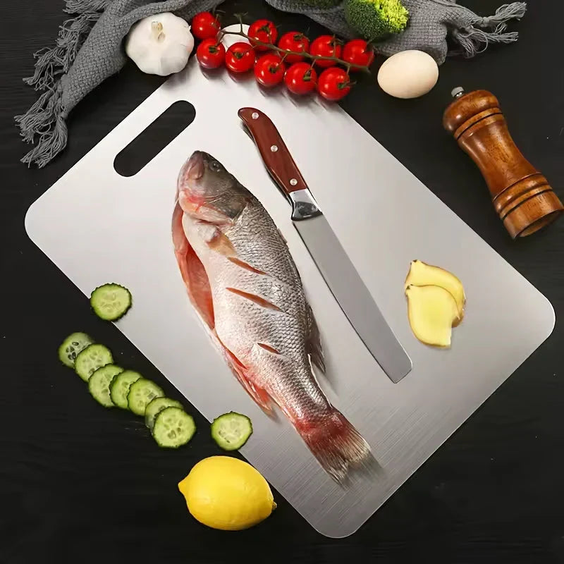 Planche métallique en vue de dessus avec un poisson entier, un couteau, des rondelles de concombre, du gingembre, des tomates et un citron autour. 5