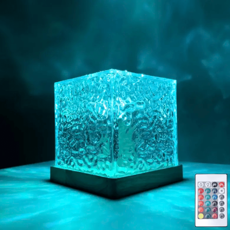 Cube de verre texturé en ondulations, allumé en turquoise sur socle en bois, avec sa télécommande posée en bas à droite. 1