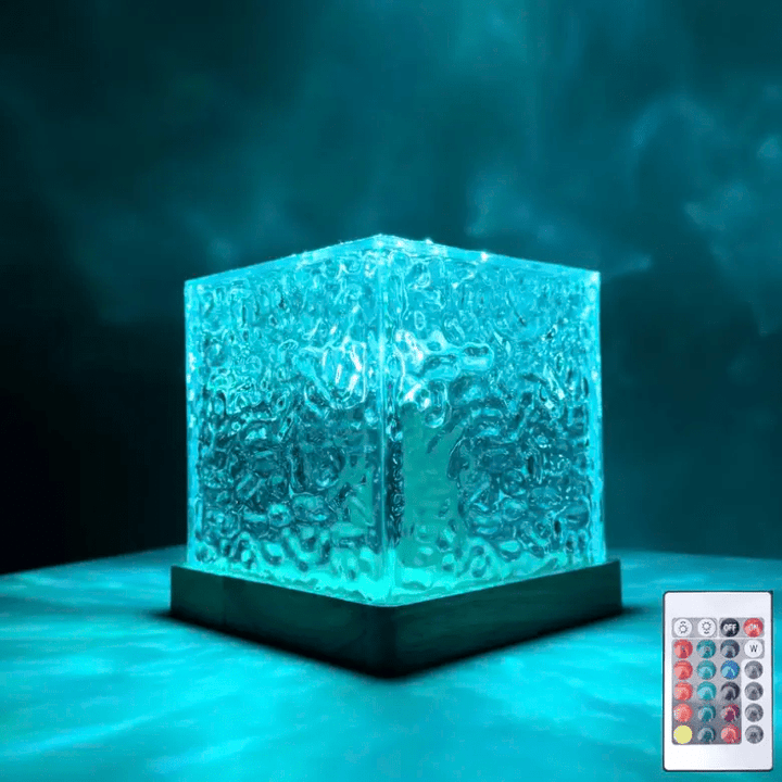 Cube de verre texturé en ondulations, allumé en turquoise sur socle en bois, avec sa télécommande posée en bas à droite. 1