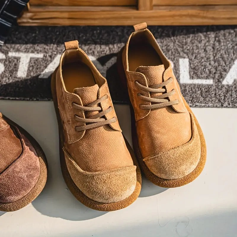 Paire de chaussures beige clair vue du dessus en légère plongée sur un sol clair, avec lacets plats et bout arrondi en daim. 2