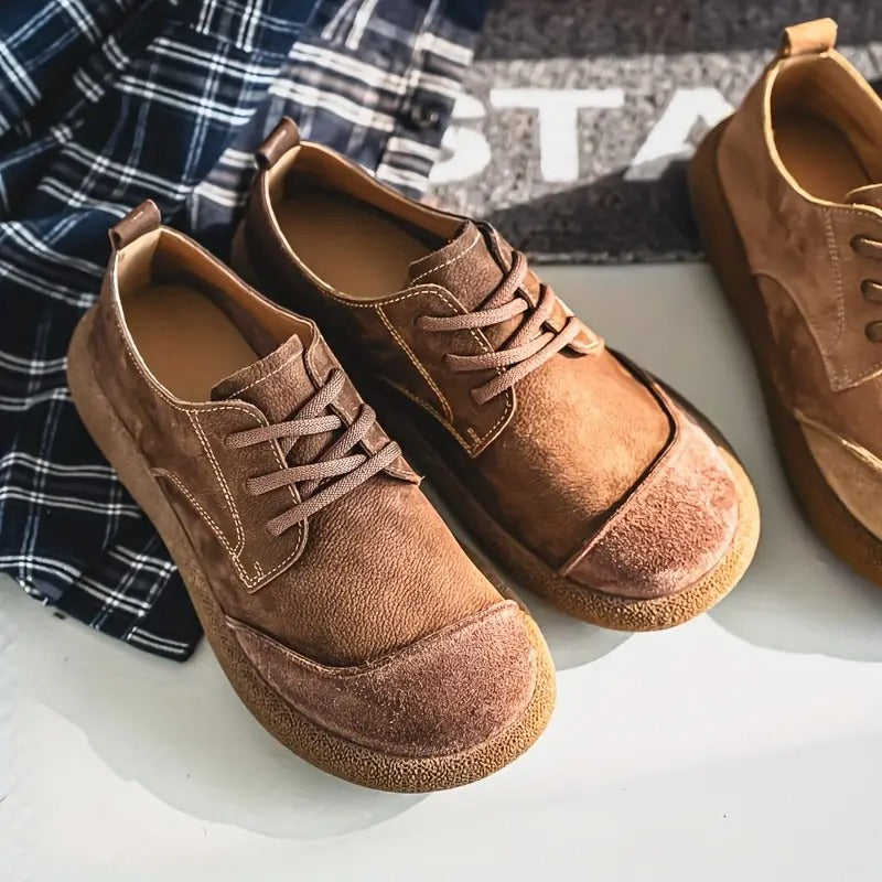 Chaussures marron et caramel posées sur une surface claire près d'une chemise à carreaux bleus, détail des coutures et du bout arrondi. 11