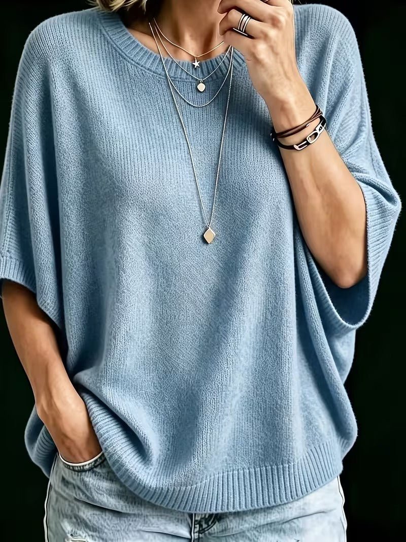 Top en maille bleu clair, plan rapproché de face, main près du col, manches amples, colliers fins et bracelets. 12