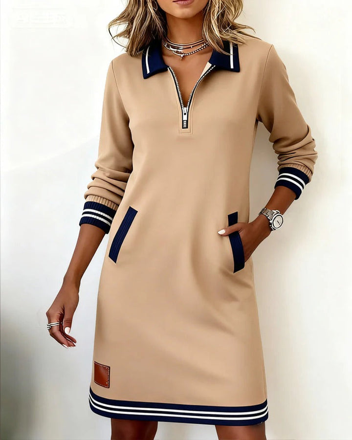Robe courte beige portée par une mannequin, une main dans la poche, avec col, poches et poignets rayés bleu marine. 3
