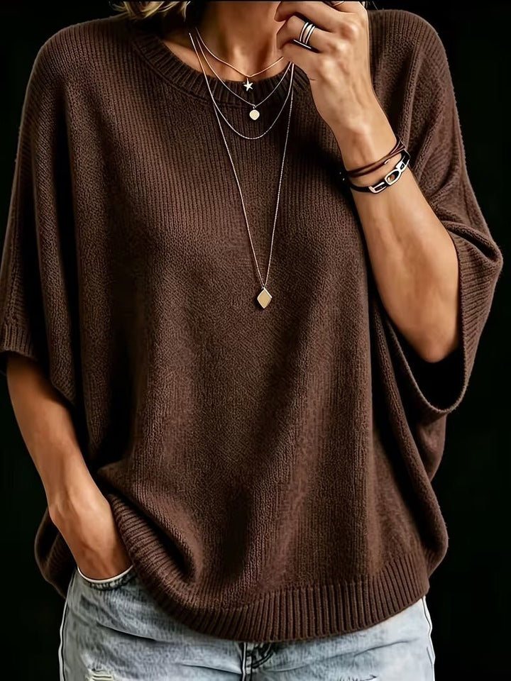 Top en maille marron, plan rapproché de face, main au col, manches amples, colliers fins et bracelets. 17