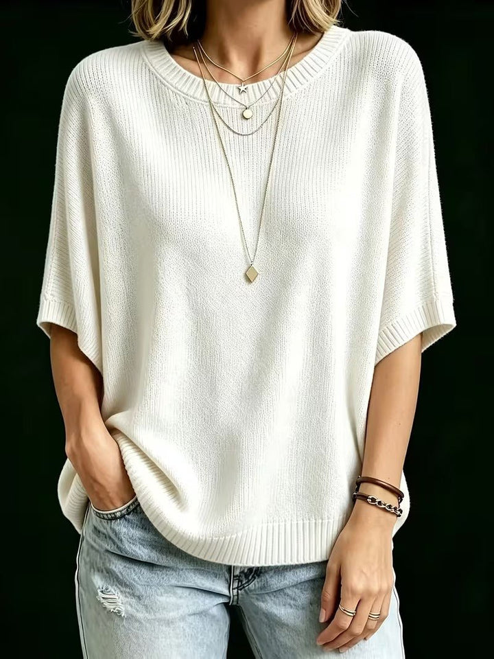 Top en maille blanc cassé porté de face avec un jean clair, une main dans la poche et des bracelets. 24