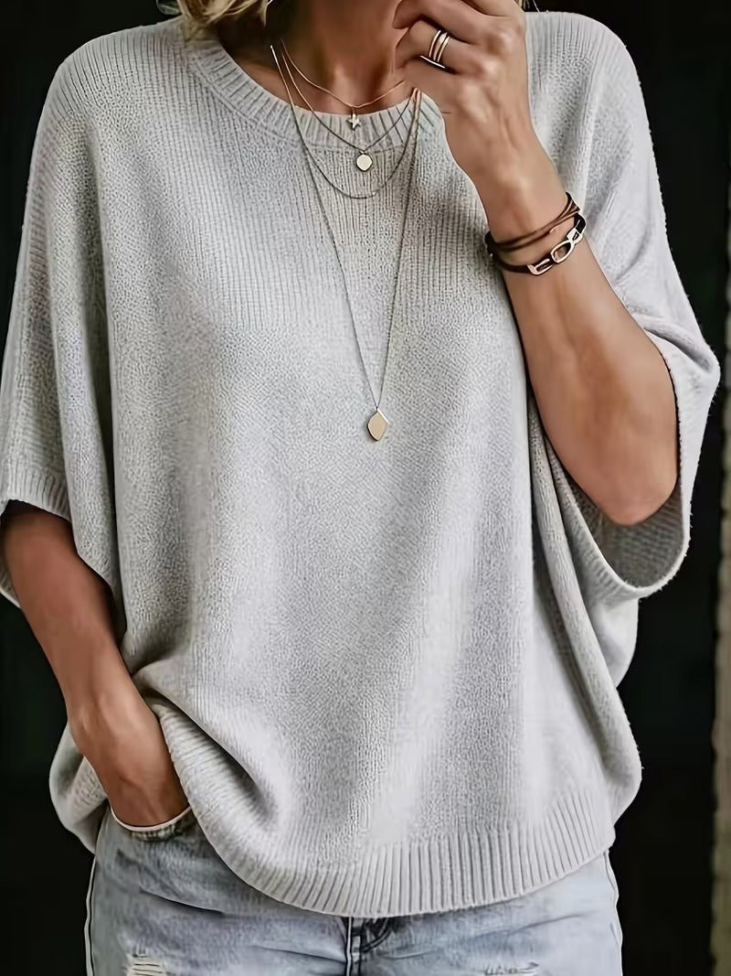 Top en maille gris clair porté avec jean, vue de face rapprochée, main vers le col, plusieurs colliers fins et bracelets. 1