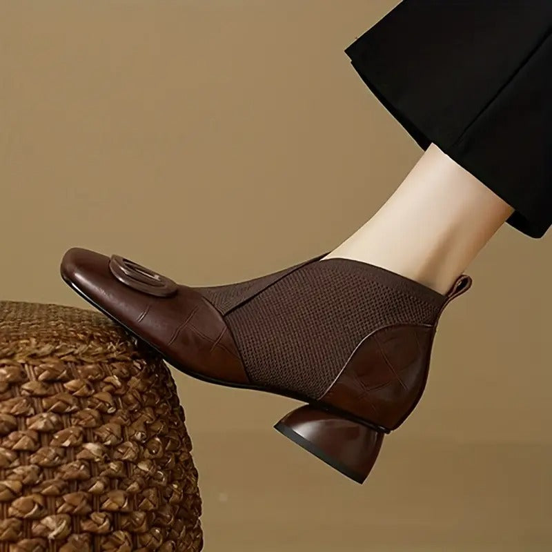 Bottine marron en cuir et maille portée, bout carré, boucle ronde et talon sculpté, posée sur un pouf tressé 1