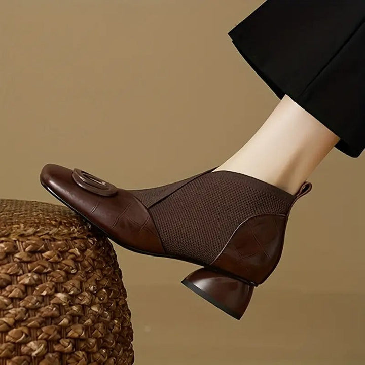 Bottine marron en cuir et maille portée, bout carré, boucle ronde et talon sculpté, posée sur un pouf tressé 1