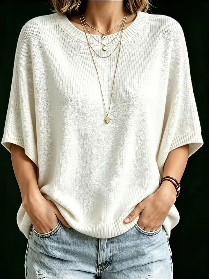 Top en maille blanc cassé vu de face, porté avec des colliers superposés, les mains dans les poches du jean. 23