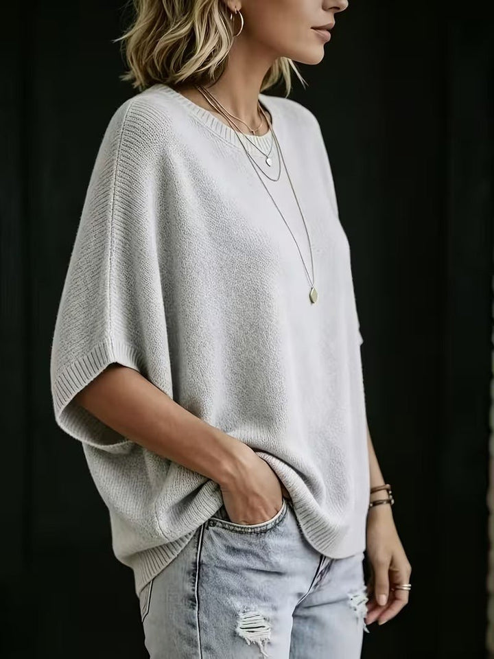 Top gris clair en maille vu de profil sur une femme, manche chauve-souris ample, main dans la poche du jean. 2