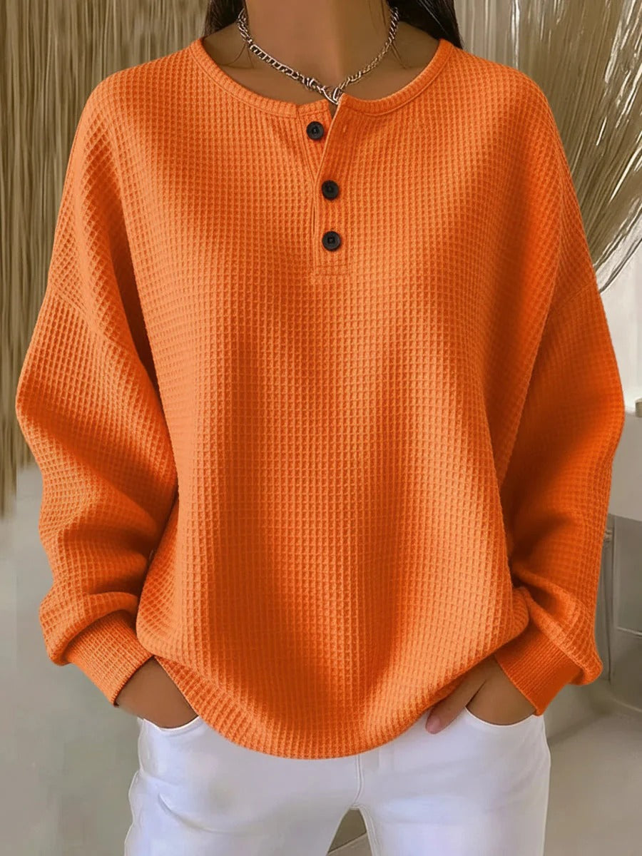 Pull gaufré orange uni à col rond et trois boutons, manches longues, porté avec un pantalon blanc. 7