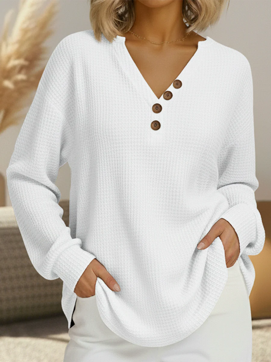 Pull gaufré blanc à col en V avec quatre boutons marron en diagonale, manches longues, main dans les poches. 12
