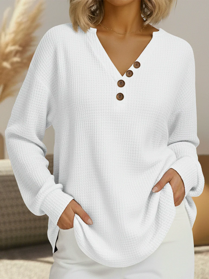 Pull gaufré blanc à col en V avec quatre boutons marron en diagonale, manches longues, main dans les poches. 12