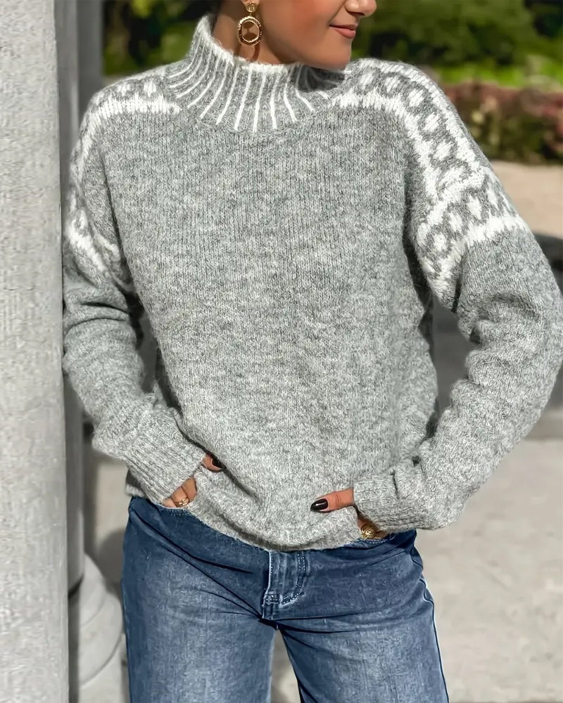 Pull en maille grise chinée à col montant, motif blanc sur les épaules, porté avec un jean bleu en extérieur. 5