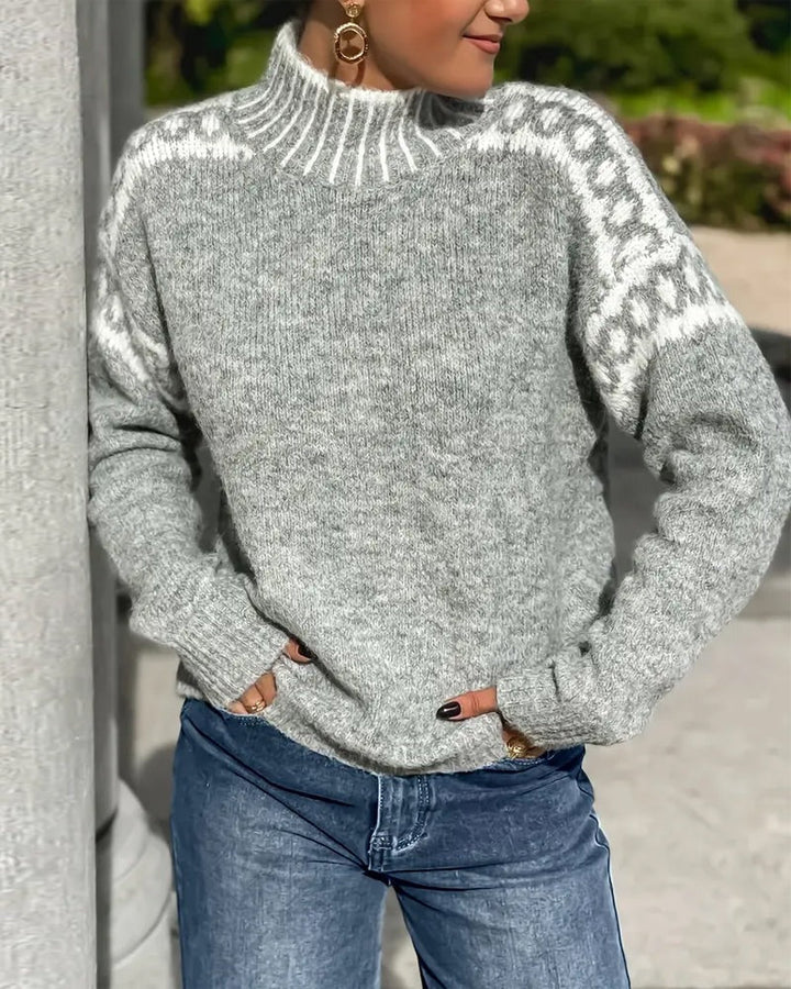 Pull en maille grise chinée à col montant, motif blanc sur les épaules, porté avec un jean bleu en extérieur. 5