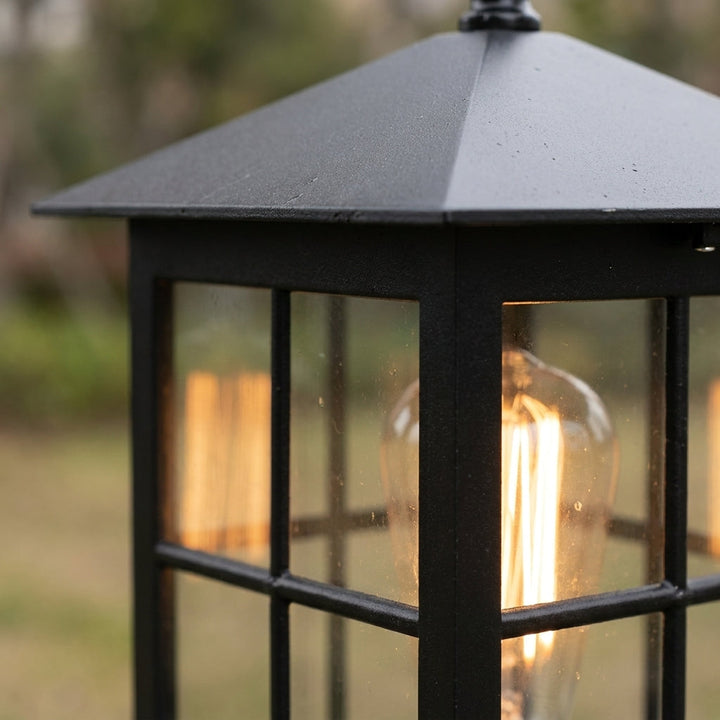 Gros plan sur le toit pyramidal et le cadre noir texturé de la lanterne, ampoule à filament allumée derrière le verre. 6