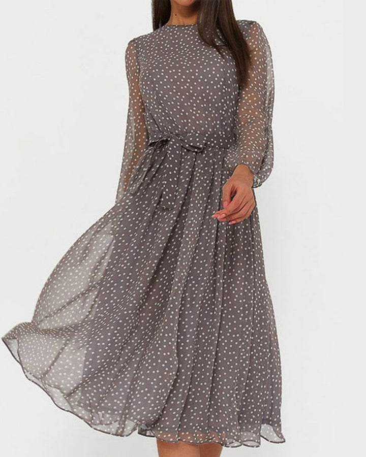 Femme portant la robe grise à pois blancs, voile léger, manches longues et ceinture nouée, sur fond uni clair. 1