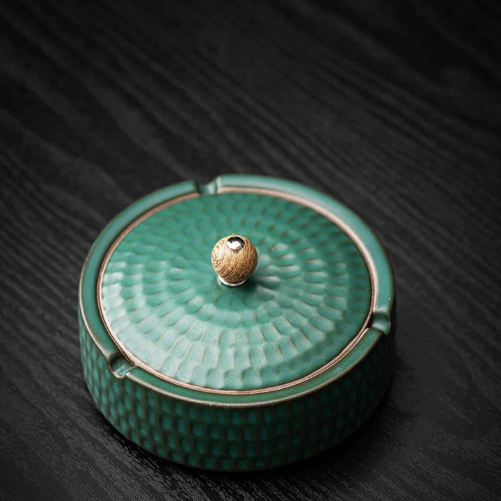 Vue de dessus du cendrier vert texturé, couvercle en place avec sa poignée en bois, posé sur une table en bois sombre. 1