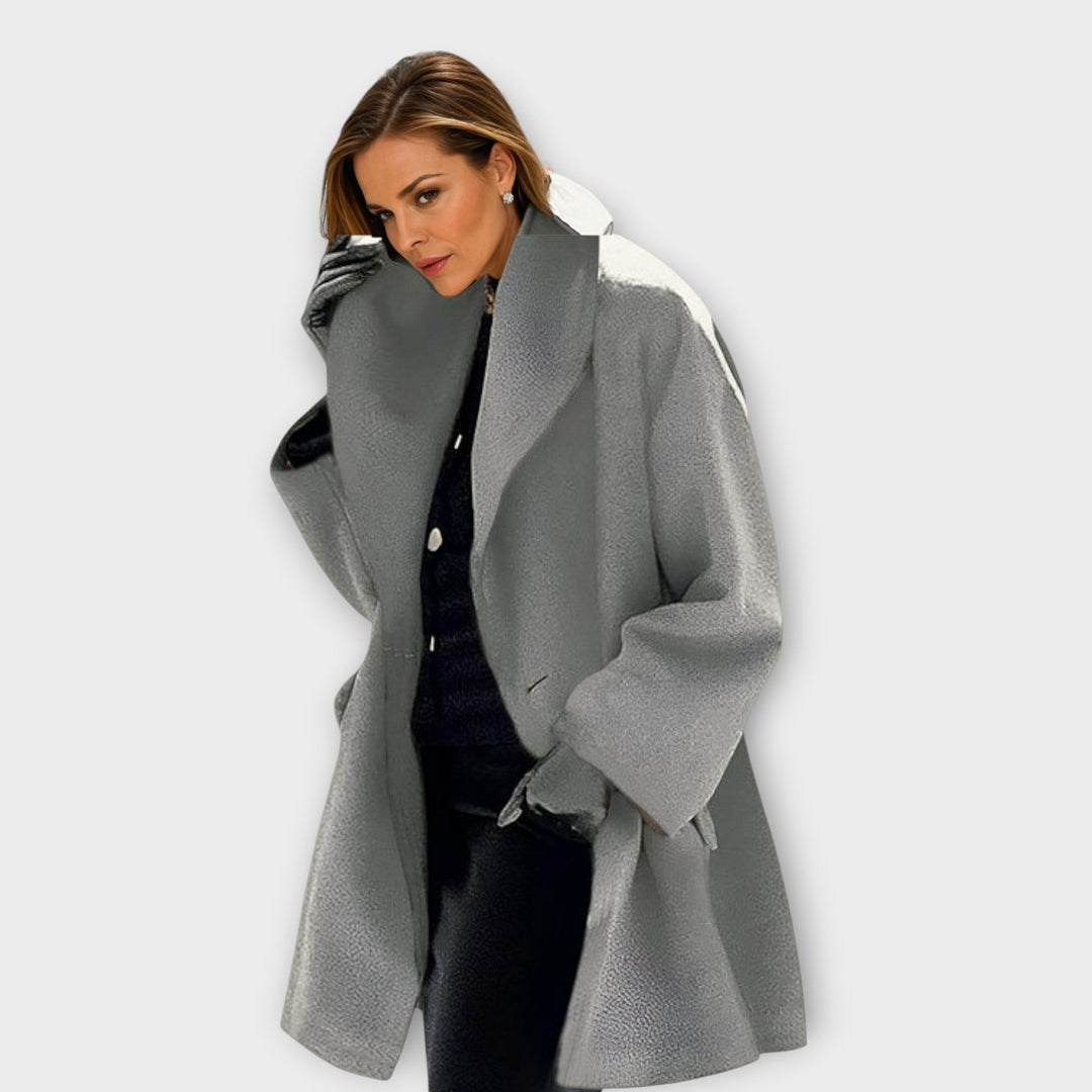 Femme en manteau gris chiné à grand col, gants noirs, ensemble foncé en dessous, pose face à l'objectif. 5