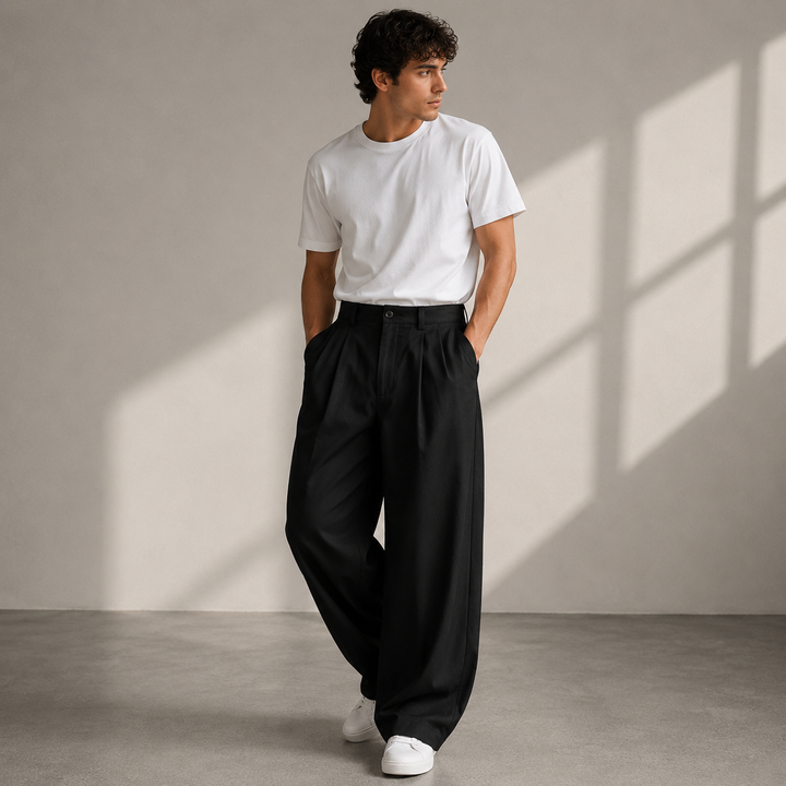 Version noire du pantalon à plis, jambes très amples, portée avec un tee-shirt blanc et des baskets blanches, mains dans les poches. 2