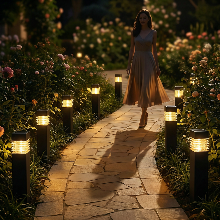 Allée de pierre sinueuse bordée de rosiers et de bornes lumineuses à la lueur chaude, avec une femme en robe au loin. 2