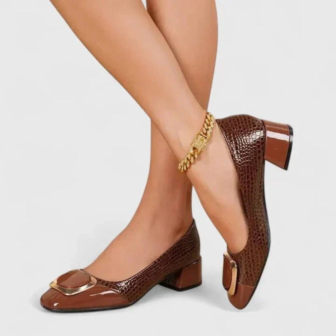 Mocassins marron portés, jambes croisées, vus de côté avec le motif croco, l'ornement doré et le talon épais. 4