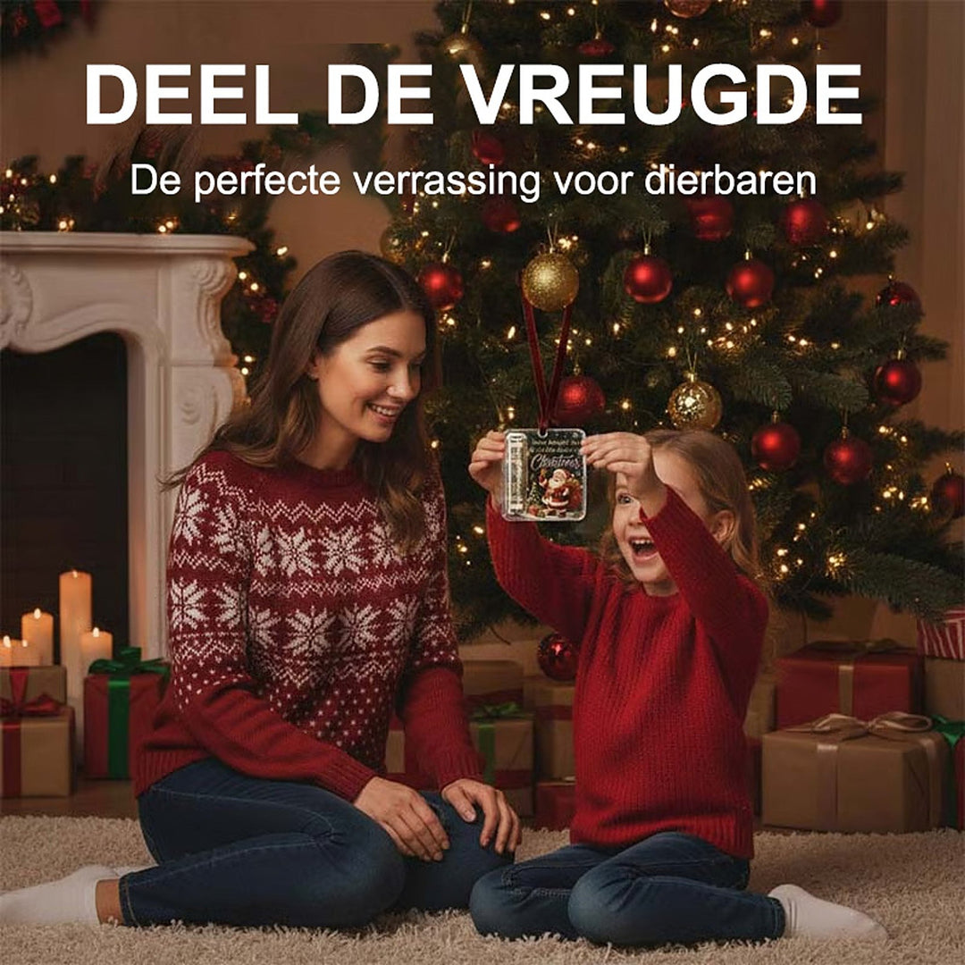 Petite fille en pull rouge brandissant la suspension en acrylique devant le sapin, sa mère souriante assise à côté d'elle. 3
