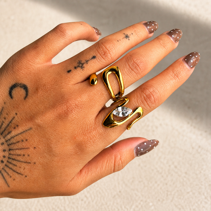 Anneau doré ouvert porté sur une main tatouée, associé à une seconde bague ornée d'une pierre claire 4