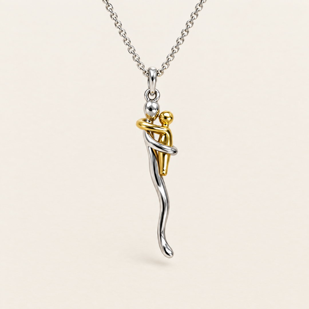 Pendentif de deux silhouettes qui s'enlacent, l'une argentée et l'autre dorée, sur une chaîne argentée, vu de face sur fond crème. 1