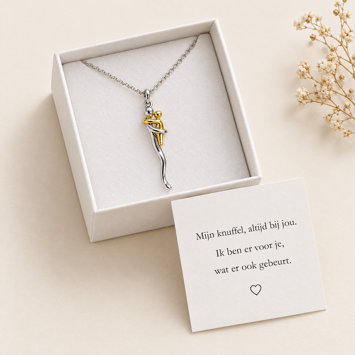 Collier présenté dans un écrin blanc ouvert avec une carte de message posée devant et une branche de fleurs séchées à côté. 2