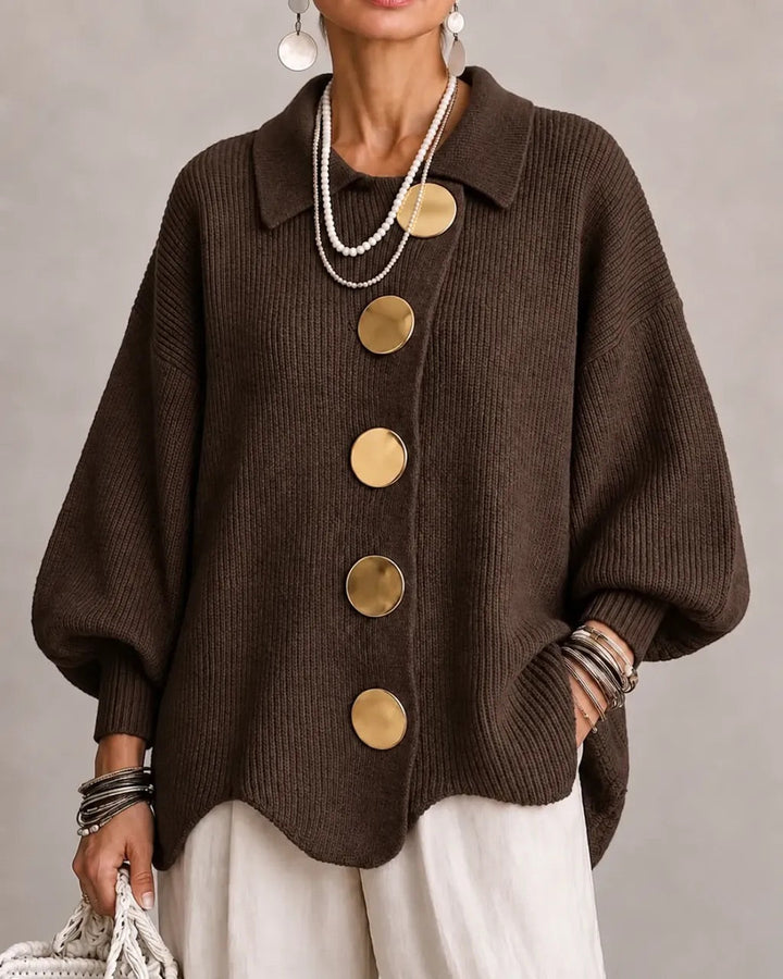 Cardigan marron chocolat à gros boutons dorés et col pointu, porté avec un pantalon blanc. 9
