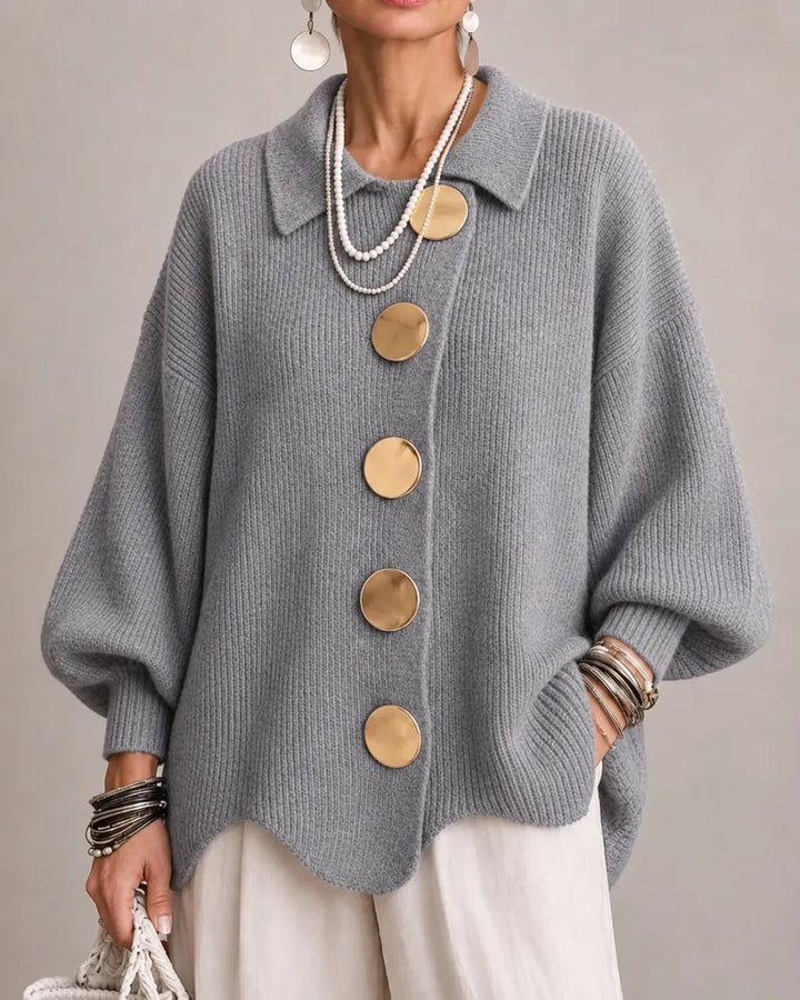 Cardigan gris moyen à gros boutons dorés et manches larges, porté avec un pantalon blanc cassé. 18