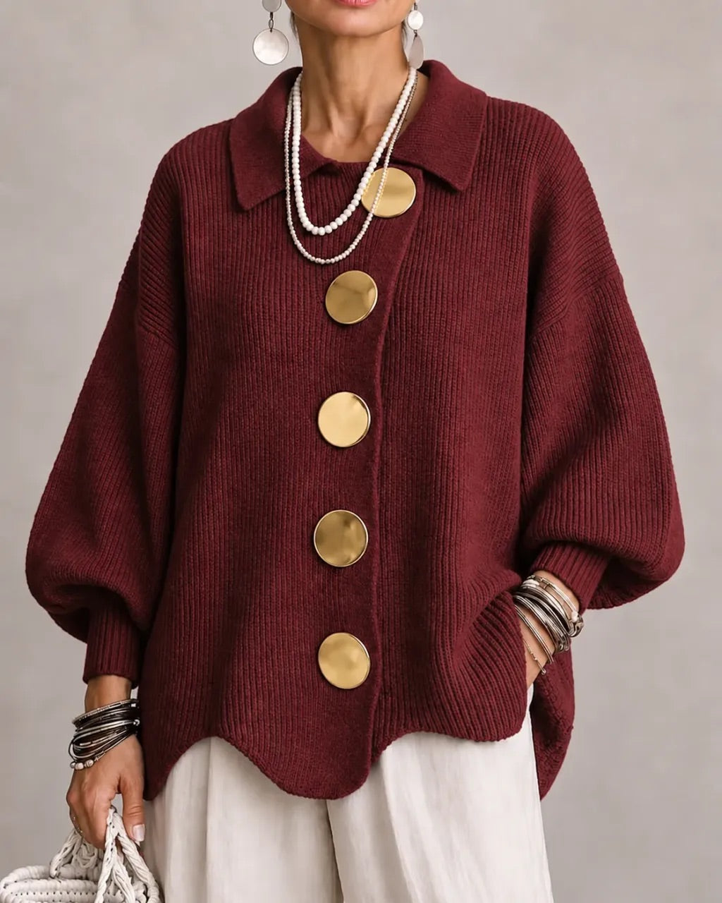 Cardigan bordeaux en maille côtelée à gros boutons dorés, porté avec un pantalon blanc et des bracelets. 19