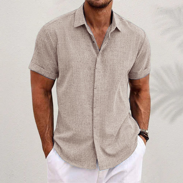 Chemise beige texturée portée par un homme en pantalon blanc devant un mur clair, avec bracelets au poignet. 2