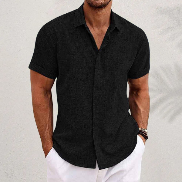 Chemise noire à manches courtes portée par un homme en pantalon blanc devant un mur clair, vue de face. 4