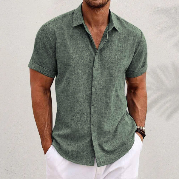 Chemise vert sauge à manches courtes, portée par un homme en pantalon blanc, mains dans les poches, vue de face. 7